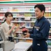 コンビニエンスストアのレジで、コーラ500mlペットボトルを手に持つ男性店長。背景には商品棚が並び、顧客が価格表示を見て驚いている様子がうかがえる。