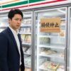 セブンイレブンの冷凍担々麺のパッケージが積まれた棚。右奥には「販売中止」と書かれた貼り紙があり、買い物客が困惑した表情で見ている。