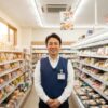 笑顔でコンビニエンスストアの通路に立つ日本人男性の店長