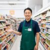 このブログの運営責任者である現役コンビニ店長の齋藤正志氏が、清潔なコンビニの店内で読者に向けてにこやかに挨拶している様子。