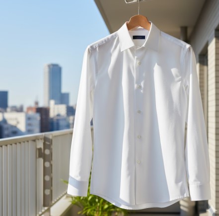 バルコニーでハンガーにかけられ、太陽の光を浴びて乾いている白い形態安定ワイシャツ。
