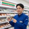 現役の日本人コンビニ店長がセブンイレブンのおにぎりを持ち、自信を持って説明している様子。