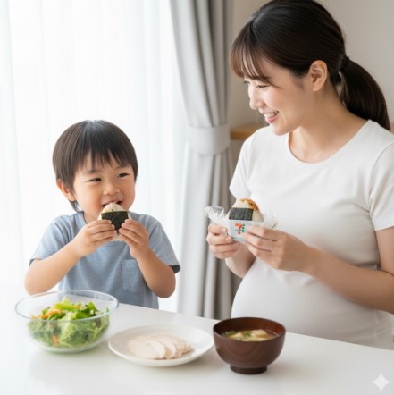 妊娠中の日本人女性と子供が、セブンイレブンのおにぎりと、サラダや味噌汁を一緒に食べている、穏やかな食事風景。