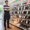コンビニの制服を着て笑顔で立っている日本人男性の店長。店内は明るく整理されており、背景にはセブンイレブンの商品棚が見える。