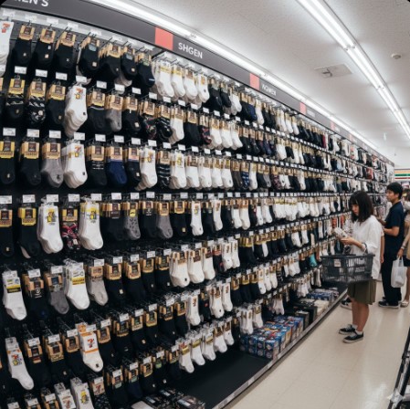 セブンイレブンの靴下売り場で、若いアジア人女性がスクールソックスや5本指ソックスを探している。