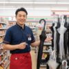 セブンイレブンの店長である齋藤正志が、店内で傘を手に笑顔で立っている。