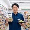 笑顔のセブンイレブン店長が、セブンプレミアムの乾麺そばのパッケージと、湯がいて盛り付けられたざるそばの器を手に持っている。背景にはコンビニエンスストアの商品棚が広がっている。