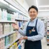 笑顔でセブンイレブンのシャンプー棚を案内する日本人男性のコンビニ店長。