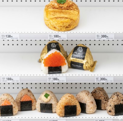 コンビニエンスストアの陳列棚に並べられた様々な種類のおにぎり。価格帯別にベーシックなものから、高級感のある「金のおむすび」、そして具だくさんのハイエンドおにぎりまでが配置されている。