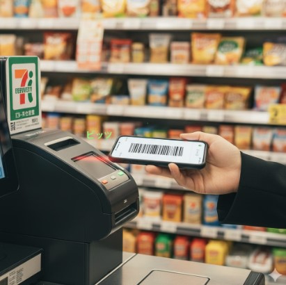 セブンイレブンのセミセルフレジでスマートフォンをかざしてバーコード決済を行う日本人女性の手。
