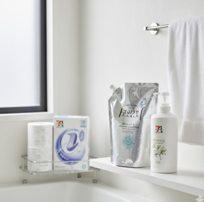 浴室の棚に置かれたセブンイレブンのボタニカルシャンプー本体と詰め替え用、奥にはトイレットペーパーと洗剤。