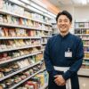 笑顔でコンビニの店内に立つ日本人男性店長。誠実な雰囲気が伝わる。