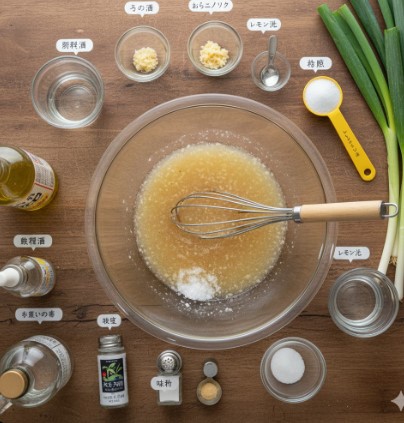 木目のテーブルに広げられた、ねぎ塩ダレの材料。中央のガラスボウルに液体調味料が入っており、その周りにネギ、レモン、ニンニク、片栗粉、砂糖、鶏ガラスープの素、味の素などの材料が小鉢や計量スプーンで配置されている。
